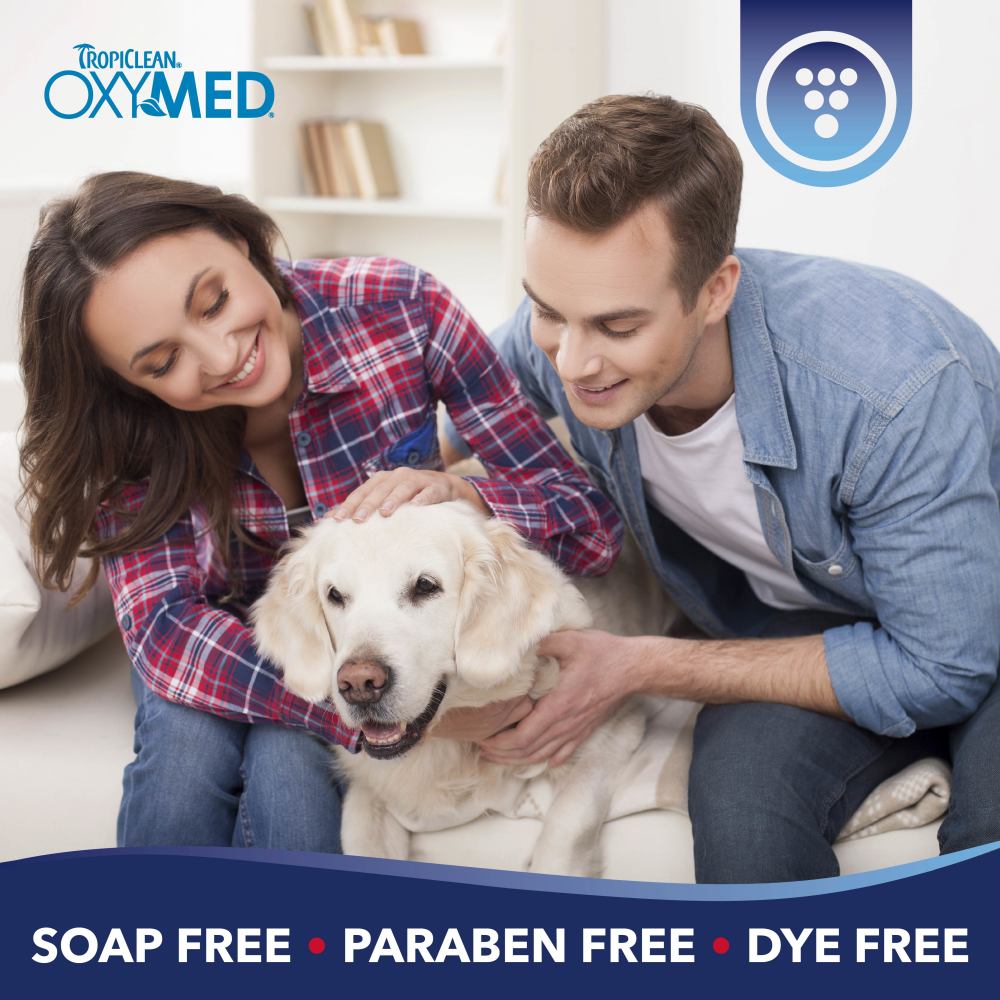 TropiClean OxyMed Ear Cleaner for Dogs and Cats. Couple with a dog on a couch, Tropiclean OxyMed branding visible