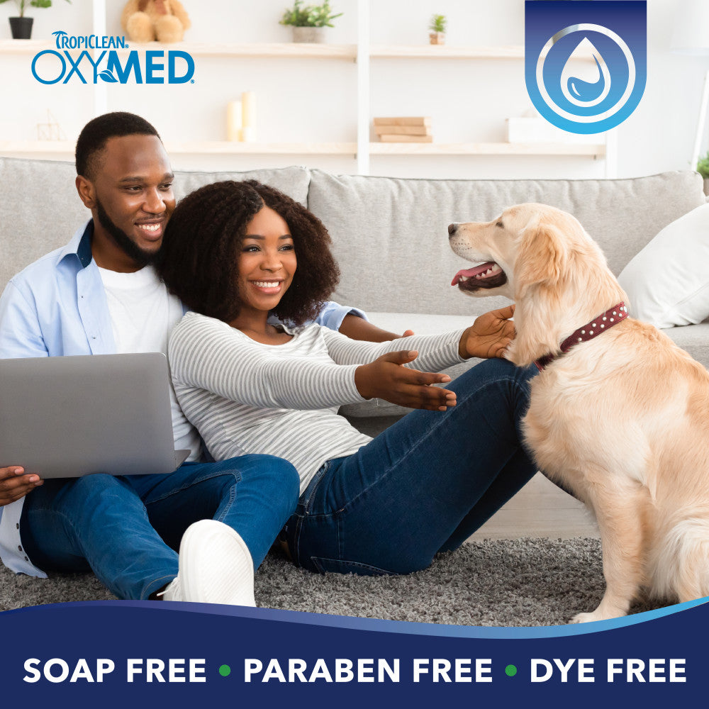 TropiClean OxyMed Hypoallergenic Oatmeal Shampoo for Dogs and Cats. Couple sitting with a dog using TropiClean OxyMed products.