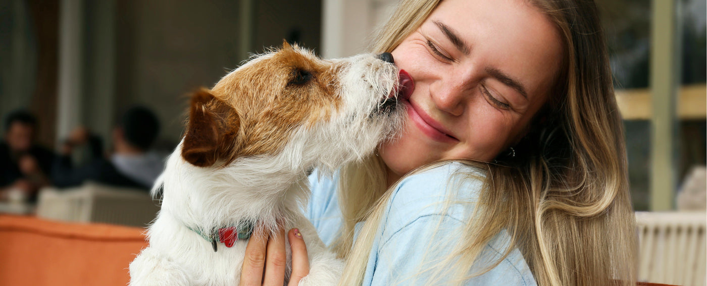 TropiClean Dental Solutions for Dogs and Cats. Dog licking a woman's face both looking happy.