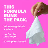 Hand holding a white wipe against a pink background with text about the product's benefits.