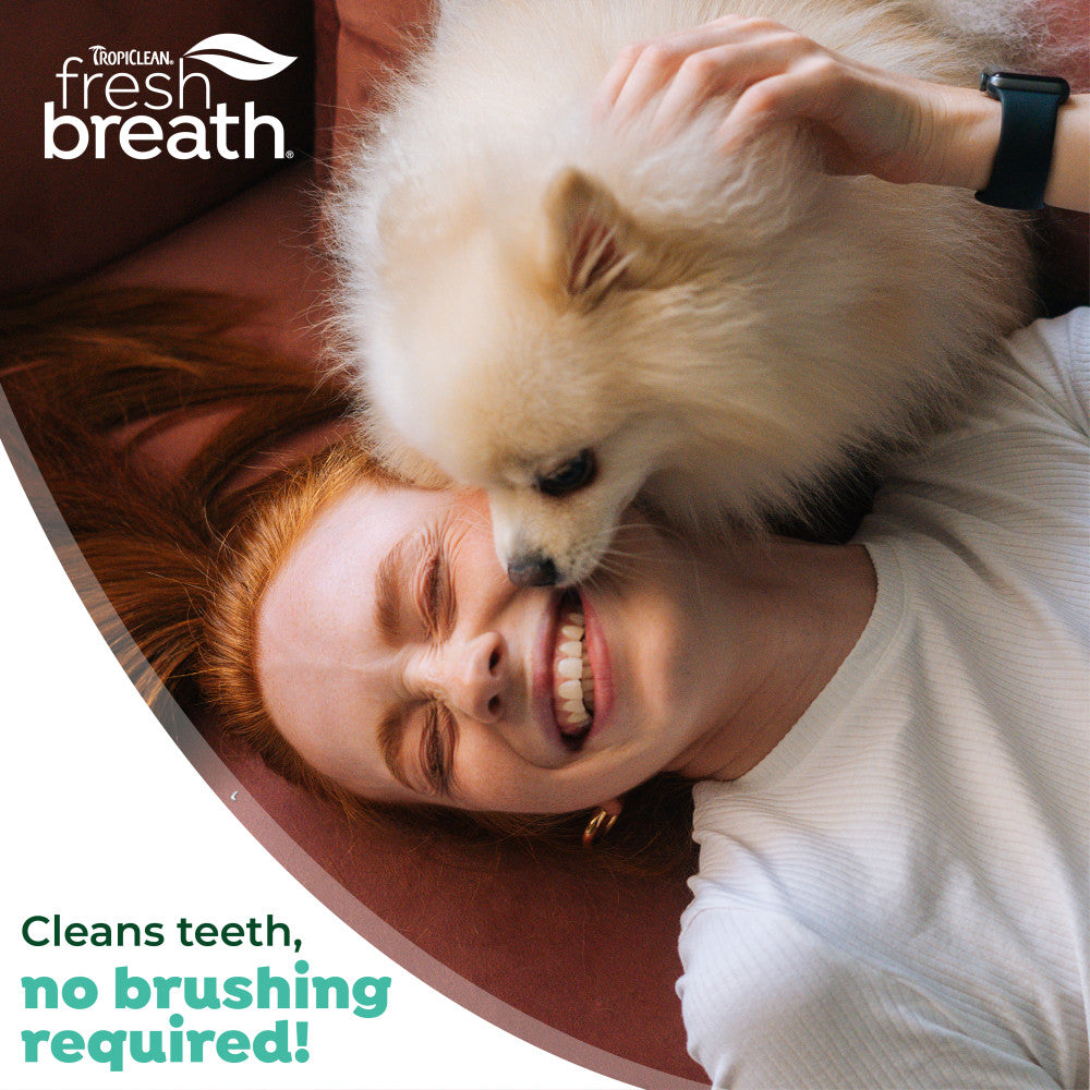 Woman lying on a couch with a small dog, promoting TropiClean Fresh Breath Dental Gel for Puppies
