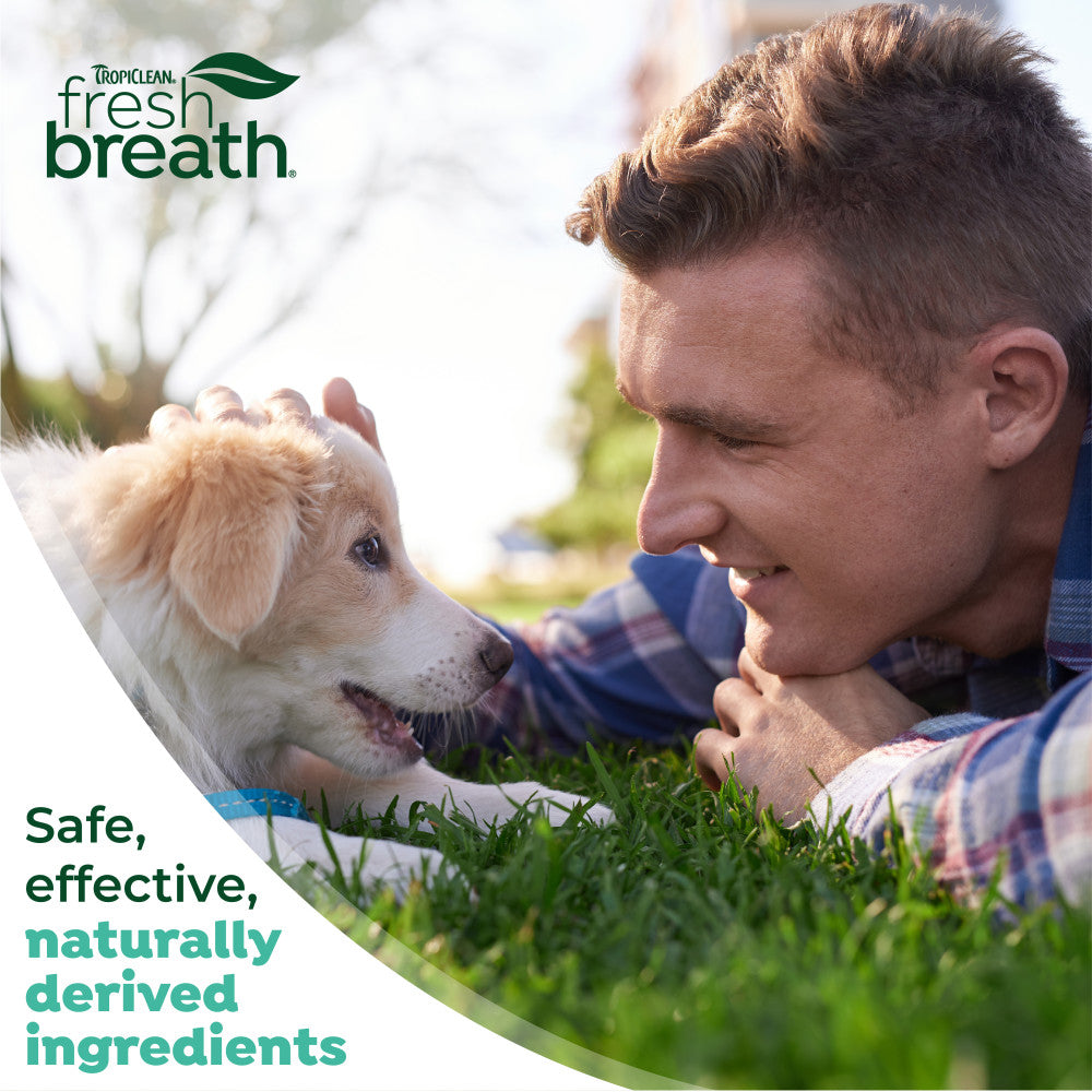 Man lying on grass with a dog, TropiClean Fresh Breath logo visible